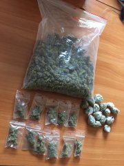 Na zdjęciu widoczna duża torebka z zapięciem strunowym z suszem roślinnym koloru zielonego obok mniejsze dilerki z narkotykami.