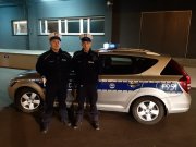 dwóch policjantów w białych czapkach stoi na tle radiowozu
