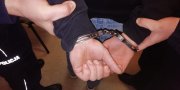 Policjanci zakładają kajdanki zatrzymanemu sprawcy