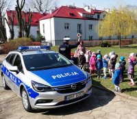 Policjanci podczas spotkania z dziećmi stoją wokół oznakowanego radiowozu