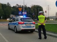 Policjant ruchu drogowego stoi przy skrzyżowaniu za radiowozem, nadzoruje bezpieczne poruszanie się uczestników imprezy sportowej