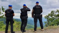 Paweł wraz z dwoma kolegami jest podczas patrolu w Kosowie. Widać na nim 3 policjantów w mundurach odwróconych tyłem do aparatu, jeden z nich patrzy przez lornetkę , w tle widać panoramę gór.