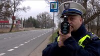 Umundurowany policjant ruchu drogowego trzyma w dłoniach urządzenie do pomiaru prędkości, którym sprawdza prędkość pojazdów na drodze.