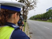Umundurowana policjantka ruchu drogowego stoi przy jezdni z urządzeniem do pomiaru prędkości