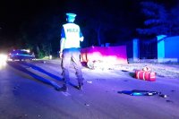 Miejsce wypadku drogowego, rozbity motocykl leży przed czerwonym parawanem, radiowóz policyjny, policjant ruchu drogowego.