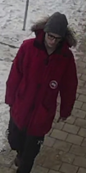 Wizerunek sprawcy kradzieży portfela. Mężczyzna w okularach, ubrany w czerwoną kurtkę z futerkiem na kapturze, szarą czapkę, czarne spodnie i ciemne buty.