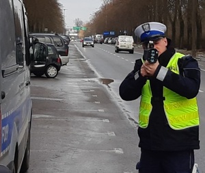 policjant w mundurze i białej czapce ruchu drogowego stojąc przy ulicy mierzy z miernika prędkości