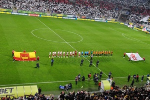Na boisku są dwie flagi ŁKS-u Łódź i miasta Łodzi. Przed meczem stoją piłkarze obydwu drużyn.