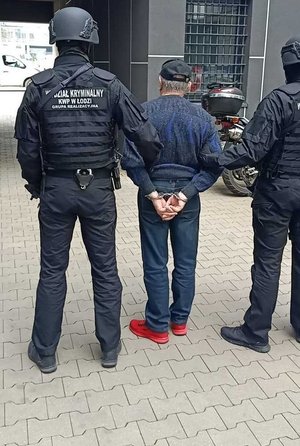 umundurowani policjanci , którzy maja napis wydział kryminalny na plecach prowadzą zatrzymanego mężczyznę