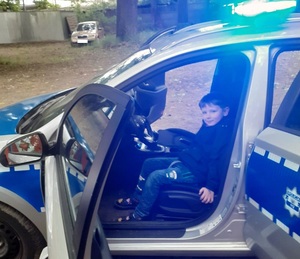Chłopiec w radiowozie policyjnym z włączonymi światłami uprzywilejowania.