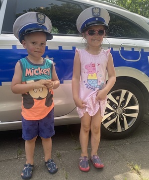 Dzieci w czapkach policyjnych na tle radiowozu