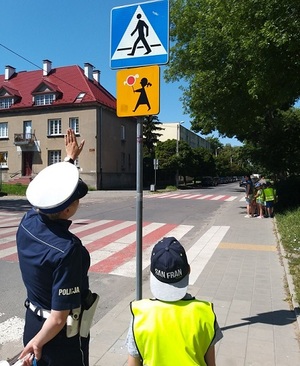 Policjantka z przedszkolakiem przed przejściem dla pieszych omawiają znaki drogowe znajdujące sie w rejonie przejścia.
