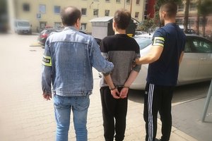 Policjanci z bałuckiego komisariatu prowadzą zatrzymanego, który ma założone kajdanki na ręce trzymane z tyłu.