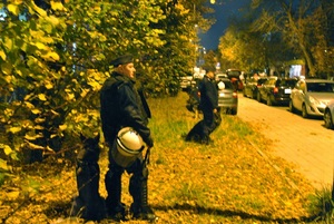 Policjant z psem służbowym przed stadionem w trakcie trwania zabezpieczenia meczu.