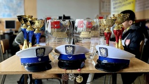 Na stole leżą medale, czapki policjantów ruchu drogowego i dalej za nimi puchary dla zwycięzców turnieju.
