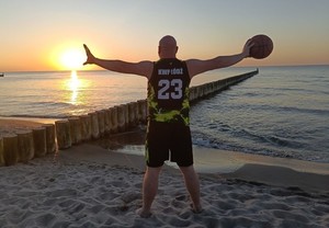 mężczyzna stoi na plaży, trzyma piłkę do koszykówki