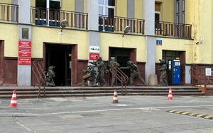 Grupa funkcjonariuszy z długa bronią stoi przed budynkiem