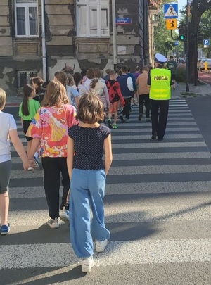 Dzieci wraz z policjantką przechodzą po pasach przez jezdnię.