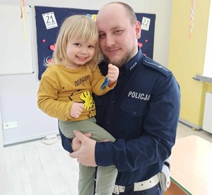 Policjant trzyma na ręku dziecko z odblaskami.