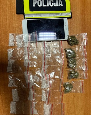 Zdjęcie poglądowe przedstawia ułożone narkotyki na biurku obok leży opaska z napisem policja.