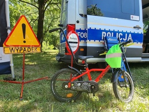 Rower na tle radiowozu policyjnego oraz znaków drogowych.