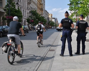 Umundurowani policjanci patrzą na przejeżdżających obok nich rowerzystów.