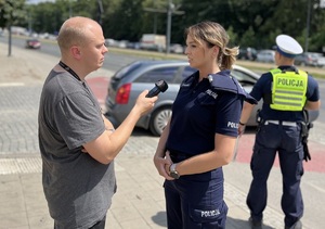 Oficer prasowy Komendanta Miejskiego Policji w Łodzi udziela komentarza dziennikarzowi odnośnie bezpieczeństwa uczestników ruchu drogowego.
