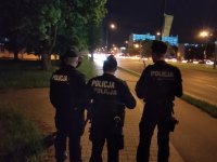 Na zdjęciu widocznych jest trzech policjantów ubranych w strój ćwiczebny nowego typu w czapkach typu &quot;furażerka&quot;. Policjanci pełnią służbę patrolową w okolicach stadionu miejskiego przy ul. Piłsudskiego w Łodzi. Zdjęcie wykonane w porze nocnej.