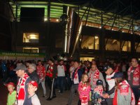 Na zdjęciu widoczna grupa kilkudziesięciu kibiców wychodząca ze stadionu po zakończeniu meczu. Kibice przemieszczają się obok pomnika &quot;z piłką&quot; znajdującego się przy stadionie. Zdjęcie wykonane zostało w porze nocnej.