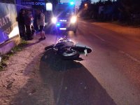 Na zdjęciu widać leżący rozbity motocykl. Obok  stoi kilka osób , którzy się przyglądają wypadkowi. Zdjęcie jest zrobione w nocy.