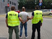 Na zdjeciu widać dwóch policjantów kamizelkach z napisem policja oraz pomiedzy nimi zatrzymany sprawca rozboju ubrany w jasna koszulke i spodnie niebieskie typu jeans.