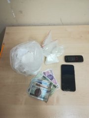 Na zdjęciu widoczna torebka z białym proszkiem (narkotyki) , dwa telefony komórkowe i kilka banknotów o nominałach 10 i 20 złotych