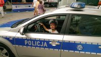 chłopiec w czapce policyjnej siedzi za kierownicą radiowozu