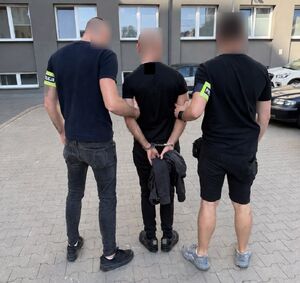 Nieumundurowani policjanci prowadzą zatrzymanego mężczyznę.