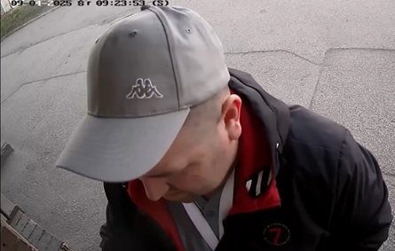  mężczyzna w wieku około 35-45 lat, szara czapka z daszkiem, granatowa kurtka z kapturem i czerwonym wnętrzem, szara koszulka, granatowe spodnie, biała smycz zawieszona na szyi, brak zarostu, krótkie włosy, na ramieniu zawieszona czarna saszetka.