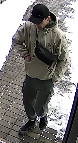 wysoki szczupły mężczyzna, w wieku około 35-45 lat, ubrany w letnią beżową kurtkę, czarną czapkę z daszkiem, przez tors ma przełożoną saszetkę typu „nerka”.