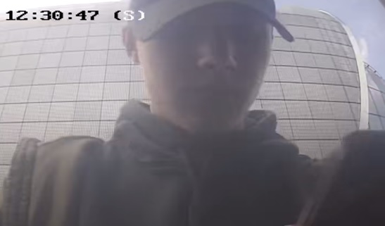 mężczyzna w wieku około 20-25 lat, ubrany w ciemną bluzę z kapturem, ciemną kurtkę, na głowie ciemna czapka z daszkiem.