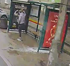 mężczyzna ubrany w szarą kurtkę na długi rękaw , szarą czapkę z pomponem w kolorze żółtym, ciemne spodnie, buty typu sportowego.