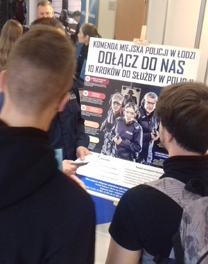 Plakat doborowy i osoby zainteresowane ofertą Policji na Targach Pracy zorganizowanych na Wydziale Zarządzania UŁ.