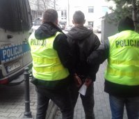 Policjanci obrani w żółte kamizelki odblaskowe z napisem Policja prowadzą zatrzymanego
