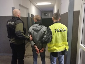 Na zdjęciu widzimy mężczyznę, którego prowadzą policjanci na korytarzu komisariatu