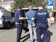 Na zdjęciu widzimy odwróconego tyłem mężczyznę, po obu jego stronach trzymają go policjanci.