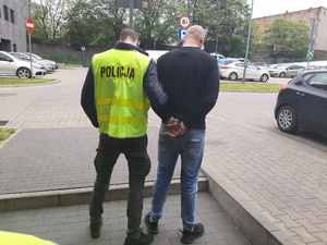zatrzymany mężczyzna którego trzyma policjant ubrany w kamizelkę policyjną.
