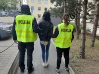 zatrzymaną &#039;kobietę trzyma policjant ubrany w żółtą kamizelkę policyjną.