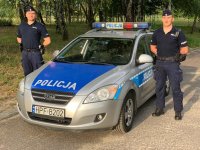 dwóch policjantów stoi po obu stronach radiowozu