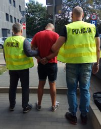 Policjanci prowadzą zatrzymanego sprawce kradzieży do radiowozu