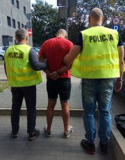 Policjanci prowadzą zatrzymanego sprawce kradzieży do radiowozu