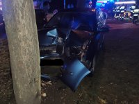 Rozbita na drzewie skoda, w tle służby tj. straż pożarna i policja [podczas czynności na miejscu zdarzenia.