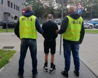 Policjanci ubrani w kamizelki z napisem POLICJA eskortują zatrzymanego mężczyznę