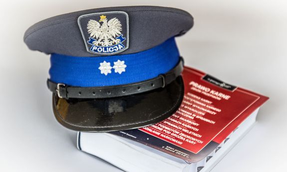 Na zdjęciu widoczny kodeks karny i położona na nim czapka policyjna